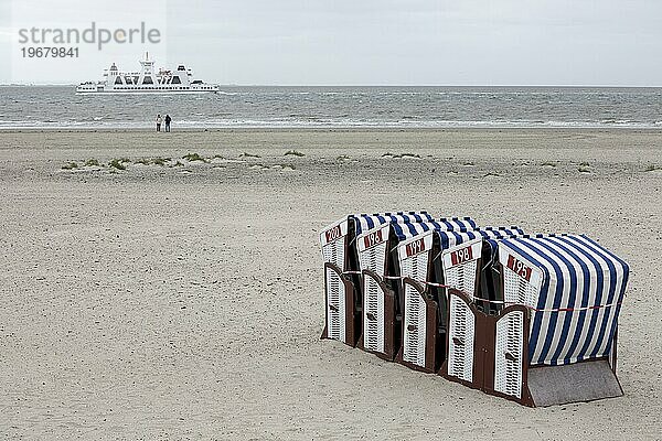 Zusammengebundene Strandkörbe am Strand mit nur zwei Menschen am Wasser und abfahrender Fähre  Saisonende  Insel Norderney  Ostfriesland  Nordsee  Niedersachsen  Deutschland  Europa