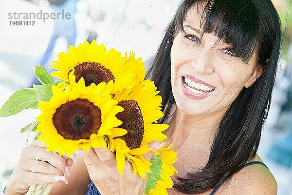 Fröhliche brünette Frau hält einen frisch geschnittenen Sonnenblumenstrauß auf dem Bauernmarkt