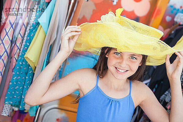 Nettes blauäugiges Mädchen modelliert spielerisch einen großen Sonnenhut auf dem Markt