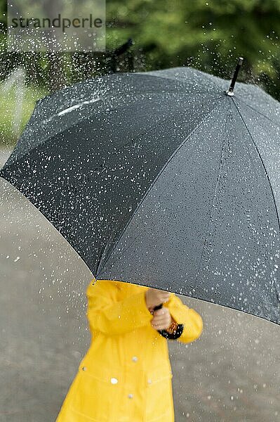 Kleines Kind hält großen schwarzen Regenschirm