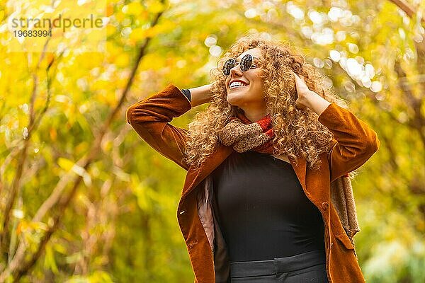 Frau mit Sonnenbrille und Freizeitkleidung schaut im Herbst in einem Park nach oben