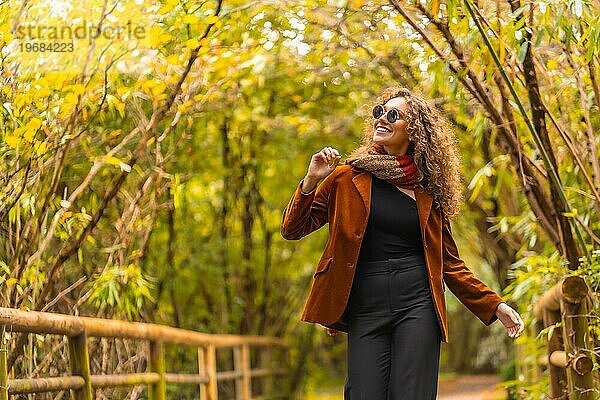 Glückliche Frau in Freizeitkleidung  die im Herbst einen Weg in einem Park entlanggeht