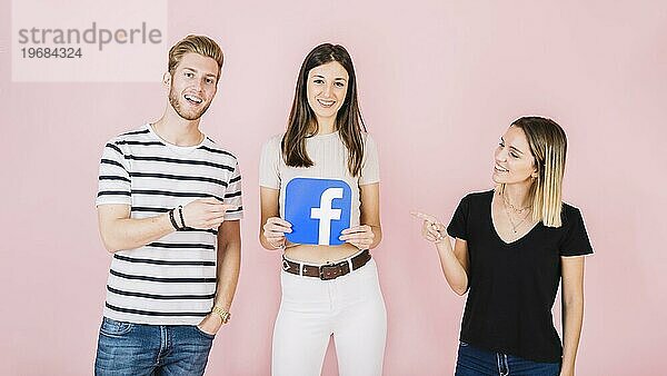Mann Frau zeigt auf ihren Freund hält Facebooksymbol rosa Kulisse