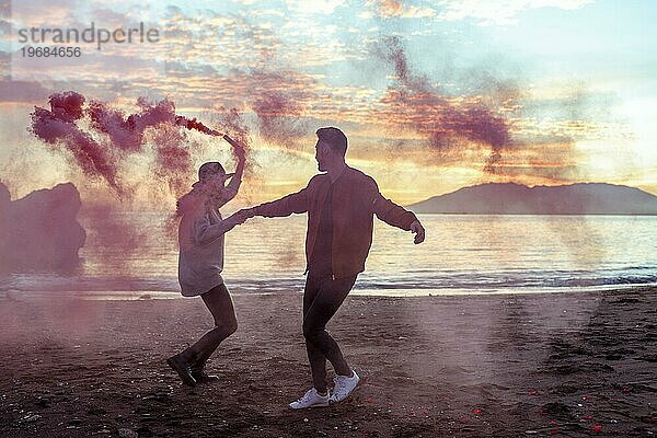 Junges Paar mit Spaß mit rosa Rauch Bombe Meer Ufer