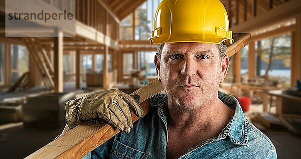 Männlicher Bauunternehmer auf einer Baustelle mit Schutzhelm und Arbeitshandschuhen  der ein 2x4 Holz hält