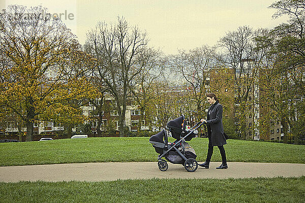 Mutter schiebt Doppelkinderwagen im Stadtpark