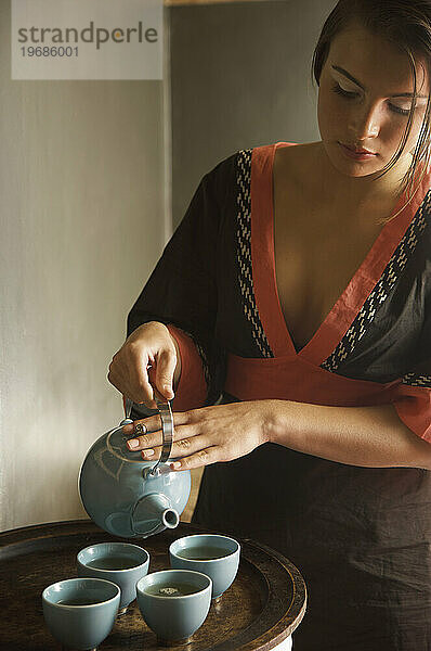 Junge Frau hält Teekanne und gießt grünen Tee ein