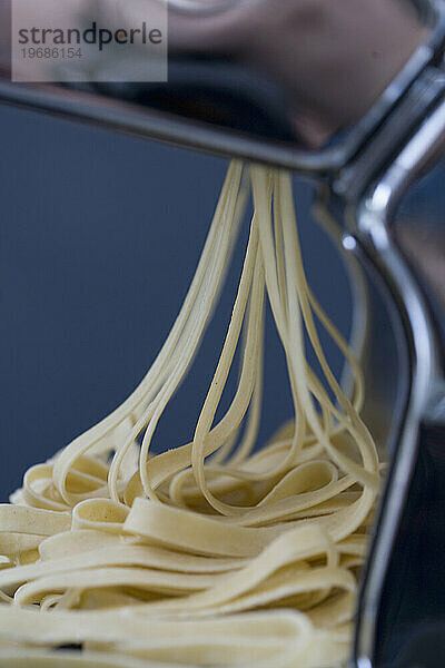 Ein Haufen frischer Tagliatelle kommt aus einer Nudelmaschine