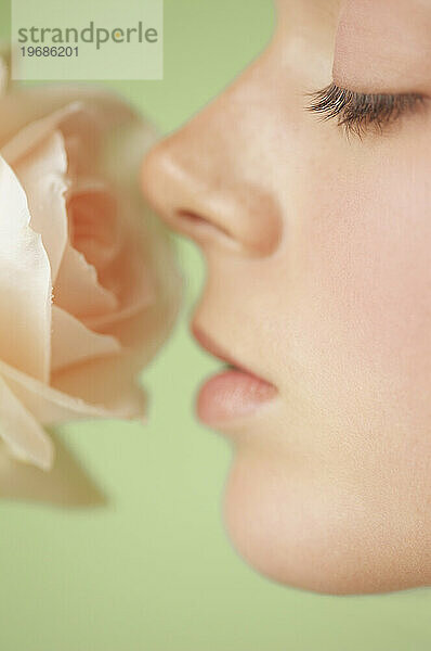 Extreme Nahaufnahme des Profils einer jungen Frau  die eine rosa Rose inhaliert