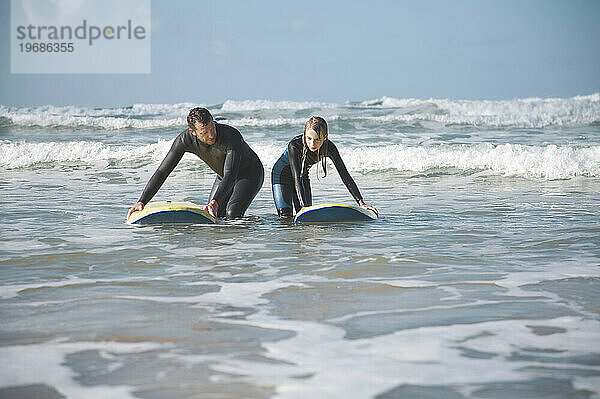 Mann und Mädchen kauern im Meer und halten sich an ihren Surfbrettern fest