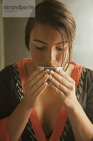Junge Frau hält Teetasse in der Hand und trinkt grünen Tee