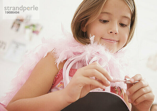 Mädchen trägt eine rosa Federboa und hält einen Lipgloss in der Hand