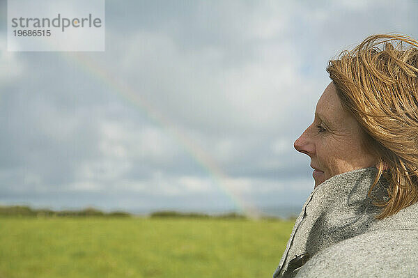 Nahaufnahme einer Frau  die auf einem Feld steht und den Regenbogen betrachtet