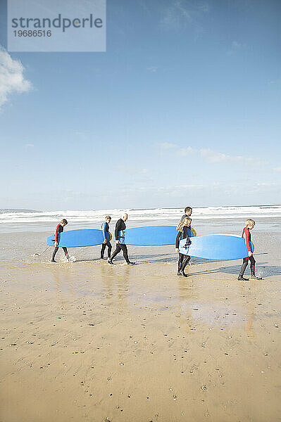Männer und Kinder gehen mit Surfbrettern am Strand spazieren