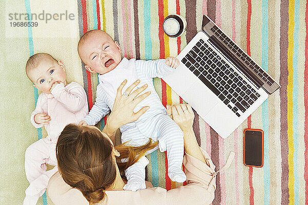 Mutter mit Zwillingsbabys liegt mit Laptop auf dem Boden  erhöhte Ansicht