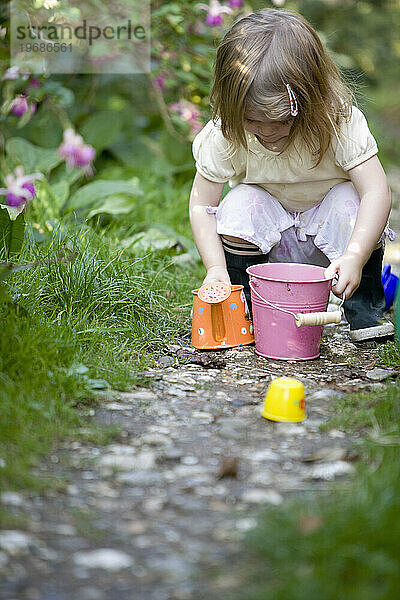 Junges Mädchen kauert in einem Garten und spielt mit Gartenspielzeug