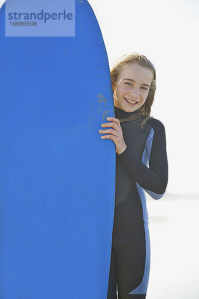 Lächelndes Mädchen  das ein Surfbrett aufrecht hält