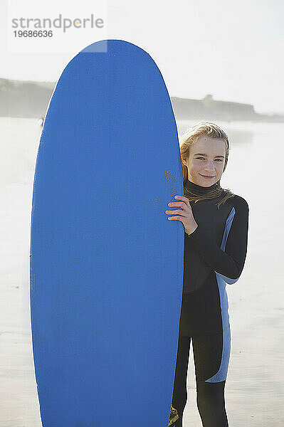 Lächelndes Mädchen  das ein Surfbrett aufrecht hält