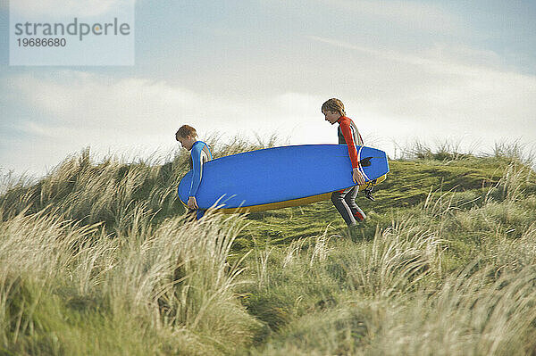 Zwei Jungen im Teenageralter laufen mit Surfbrettern auf einer Sanddüne
