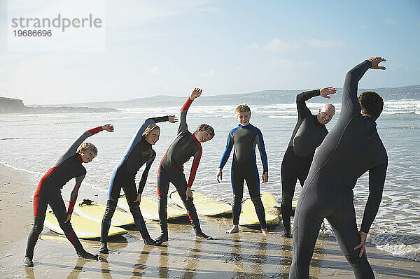 Rückansicht eines Surflehrers und einer Gruppe von Schülern  die sich am Strand dehnen