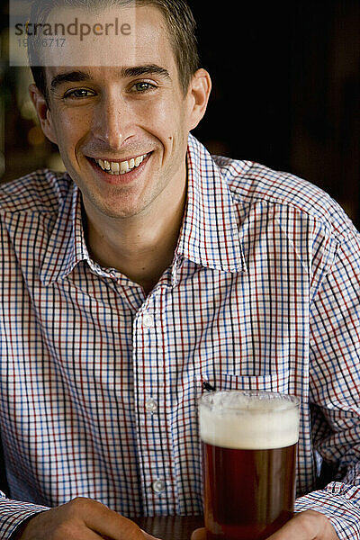 Lächelnder Mann sitzt und hält ein Pint Bier