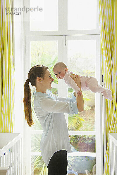 Mutter hebt Baby im Kinderzimmer hoch