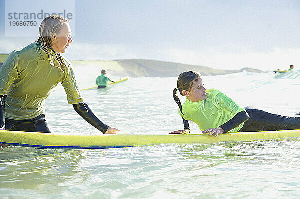 Frau im Meer hält ein Surfbrett  auf dem ein Mädchen liegt