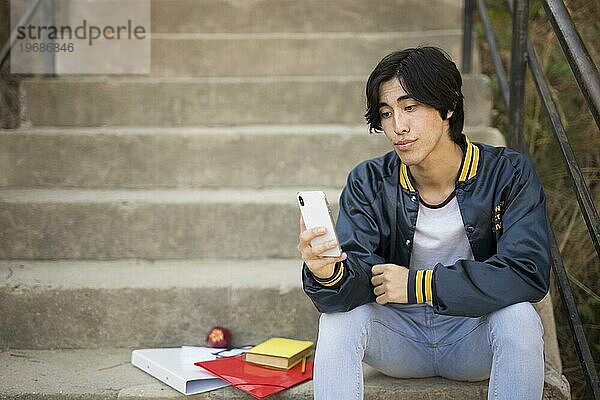 Asiatischer Teenager sitzend mit Telefontreppe