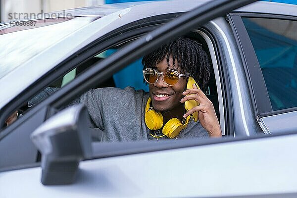 Cooler afrikanischer junger Mann  der in einem Auto sitzend telefoniert