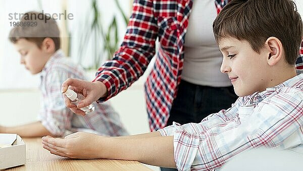 Seitenansicht Mutter sprüht Desinfektionsmittel auf die Hände des Kindes