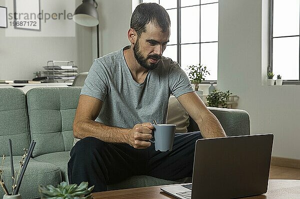 Mann trinkt Kaffee bei der Arbeit von zu Hause aus Laptop