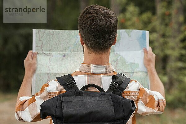 Rückenansicht Mann mit Rucksack schaut Karte beim Camping