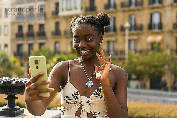 Junge niedliche afrikanische Frau winkt während eines Videoanrufs mit dem Mobiltelefon auf der Straße