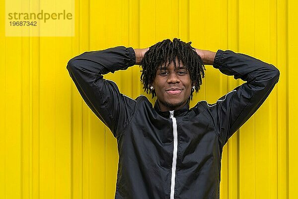 Lächelnder junger afrikanischer Mann posiert entspannt im Freien neben einem städtischen gelben Hintergrund