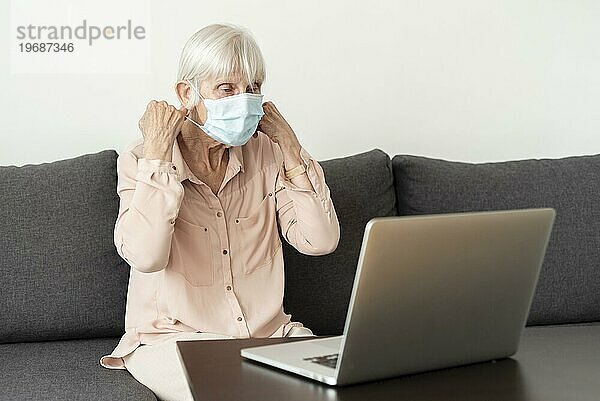 Seitenansicht ältere Frau mit Laptop setzt medizinische Maske