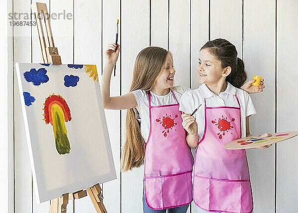 Portrait lächelnd zwei Mädchen rosa Schürze macht Spaß beim Malen Leinwand