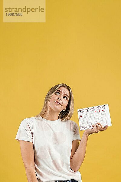 Frau blickt auf und hält einen Menstruationskalender