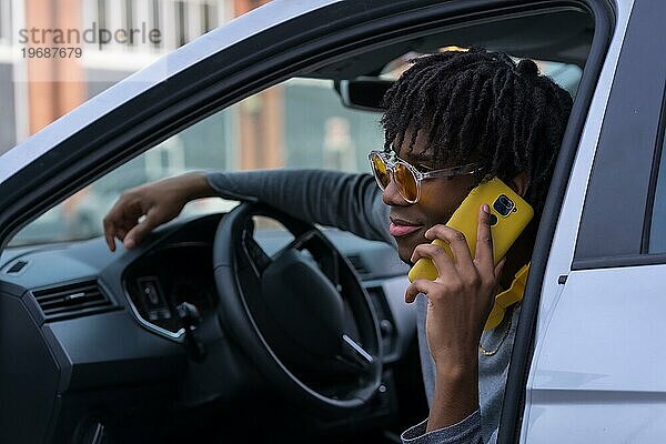 Cooler afrikanischer junger Mann  der auf einem Auto sitzend telefoniert