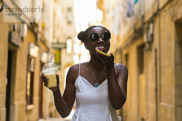 Frontalporträt einer jungen afrikanischen Frau  die einen Milchshake auf der Straße genießt