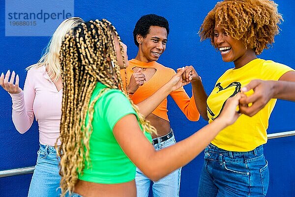 Lateinamerikanische und afrikanische Frau tanzt zusammen mit Freunden Salsa vor einem blauen Hintergrund