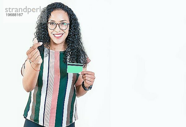 Glückliches afroamerikanisches Mädchen mit Brille  das eine Kreditkarte hält und mit den Fingern eine Geldgeste macht  schaut in die Kamera  isoliert