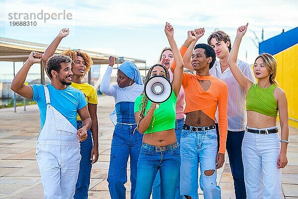 Multikulturelle und geschlechtsspezifische junge Menschen  die bei einer Protestaktion in einem städtischen Raum über einen Lautsprecher schreien