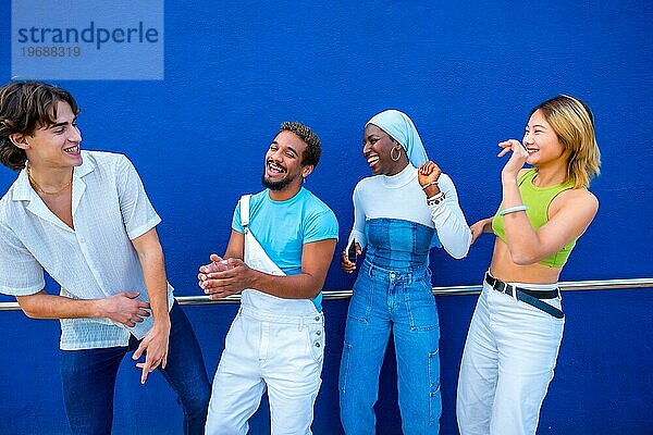 Frontalansicht von vier multiethnischen Freunden  die sich beim Tanzen neben einer blauen Wand amüsieren