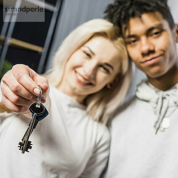 Freundin mit ihrem Freund zeigt Hausschlüssel in Richtung Kamera