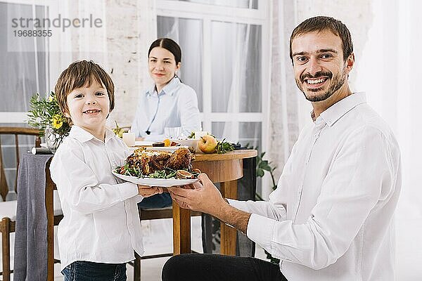 Glücklicher Mann mit Sohn  der einen Teller mit Hühnchen hält