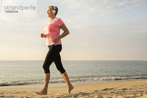 Seitenansicht ältere Frau mit Kopfhörer joggen Strand