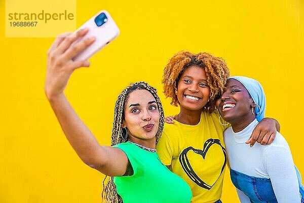 Porträt mit Kopiervorlage von drei Freundinnen  die zusammen ein Selfie vor einem gelben Hintergrund machen