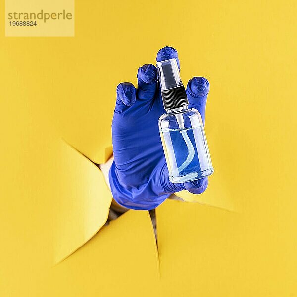 Vorderansicht einer Hand mit chirurgischem Handschuh  die eine Handdesinfektionsmittelflasche hält