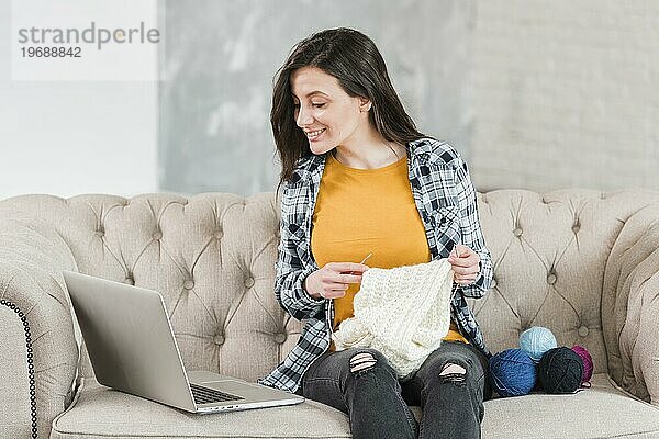Frau strickend mit Blick auf Laptop