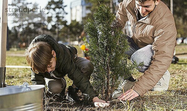 Kleiner Junge und sein Vater pflanzen einen Baum im Freien